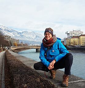 Student sitting on a stone wall in front of water with mountains in the background