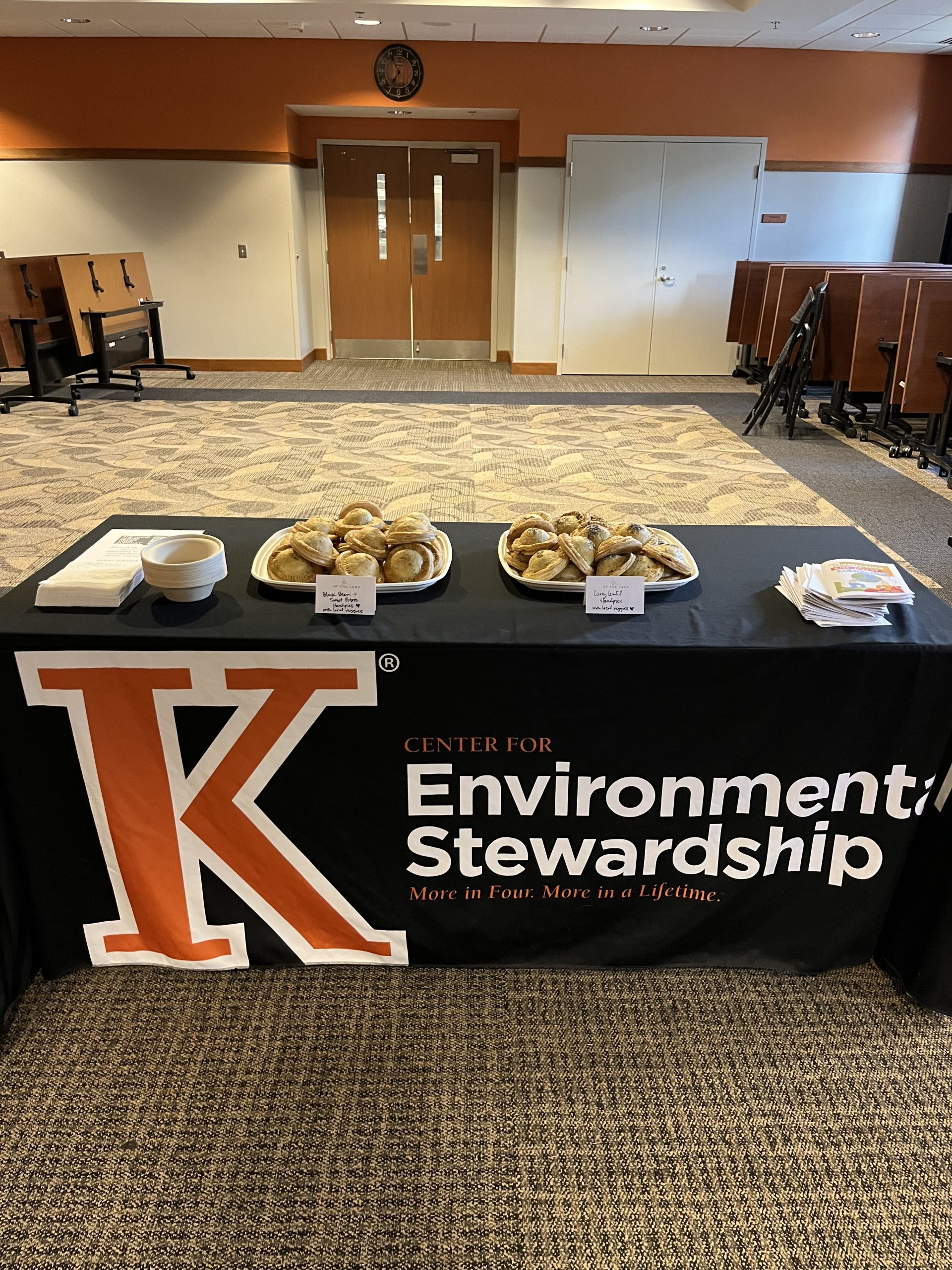 Black table cloth with an orange K that reads Environmental Stewardship. Pastries are on top of the table