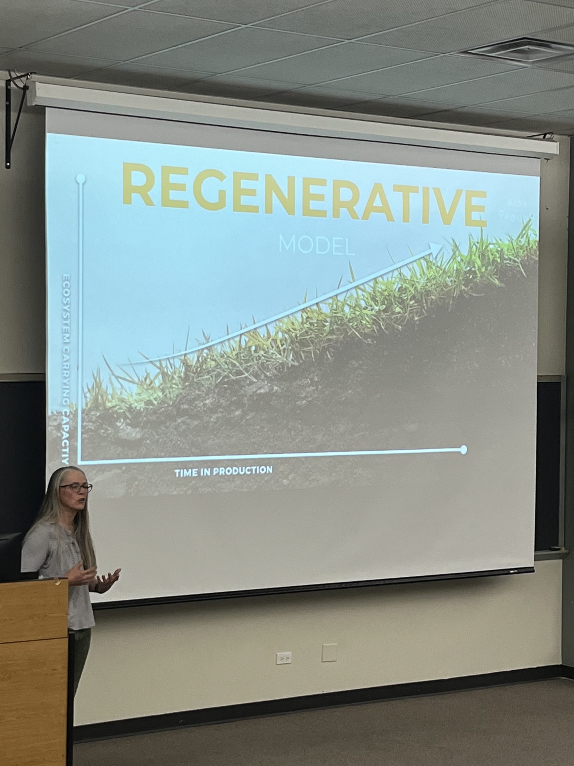 Kirsten Clemente standing in front of a large projection screen giving a presentation on regenerative agriculture