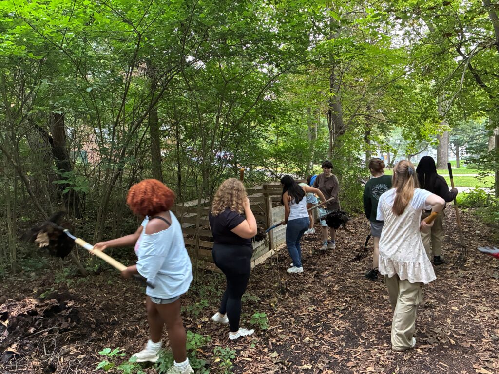 Students shoveling dirt and compost in a wooded area