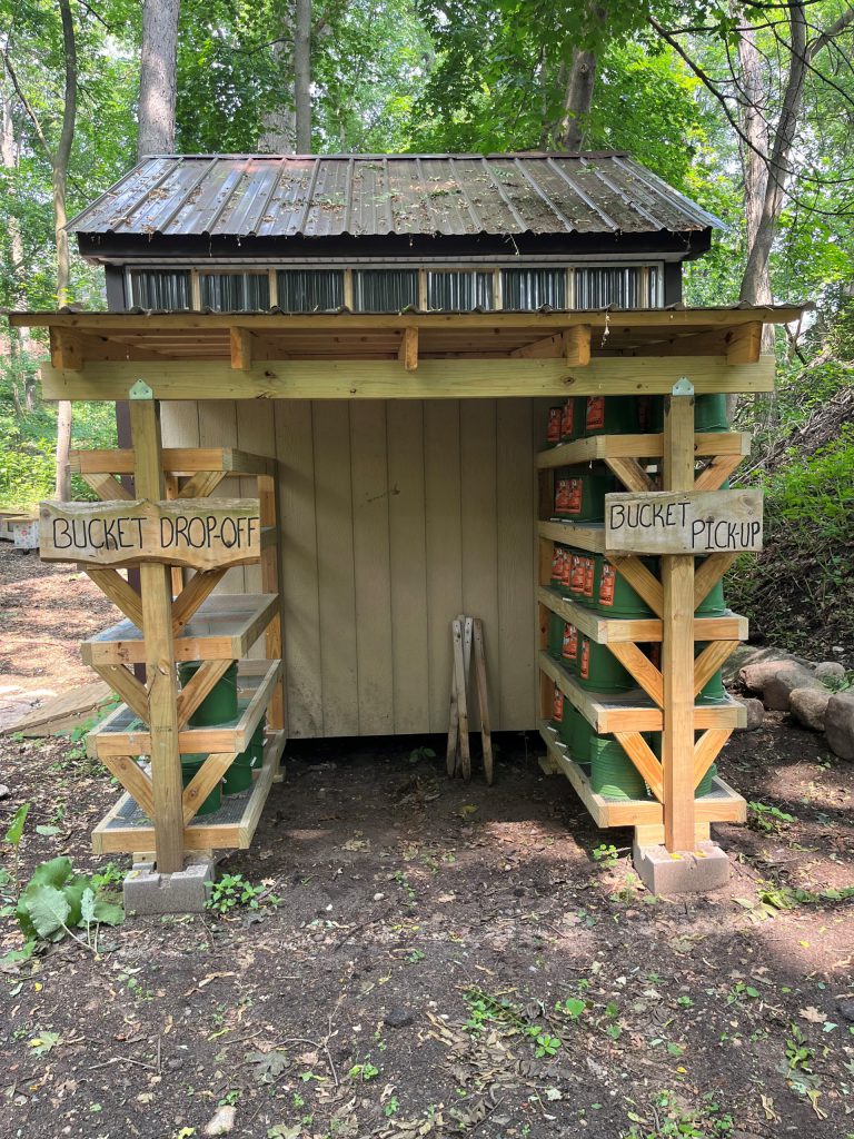 shed in the woods with shelves that say bucket drop off and bucket pick up